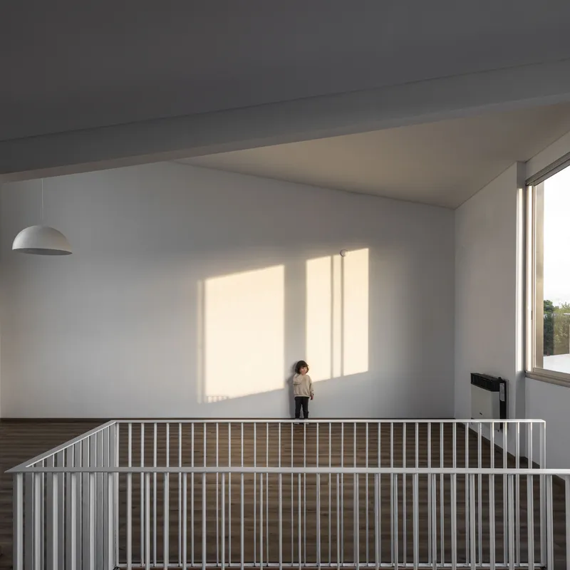 Upper floor room with white walls and slatted railing where child stands in afternoon sunlight