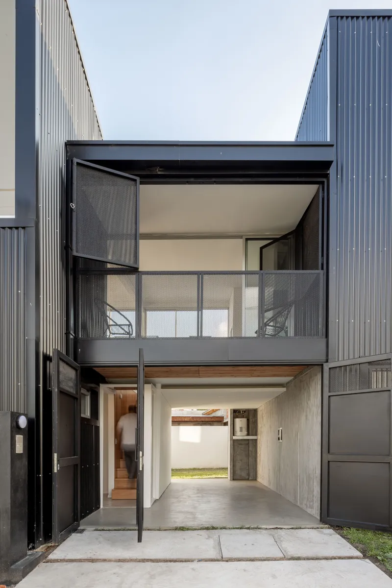 Entry courtyard with pivoting metal door, concrete paving and an upper balcony with mesh railing