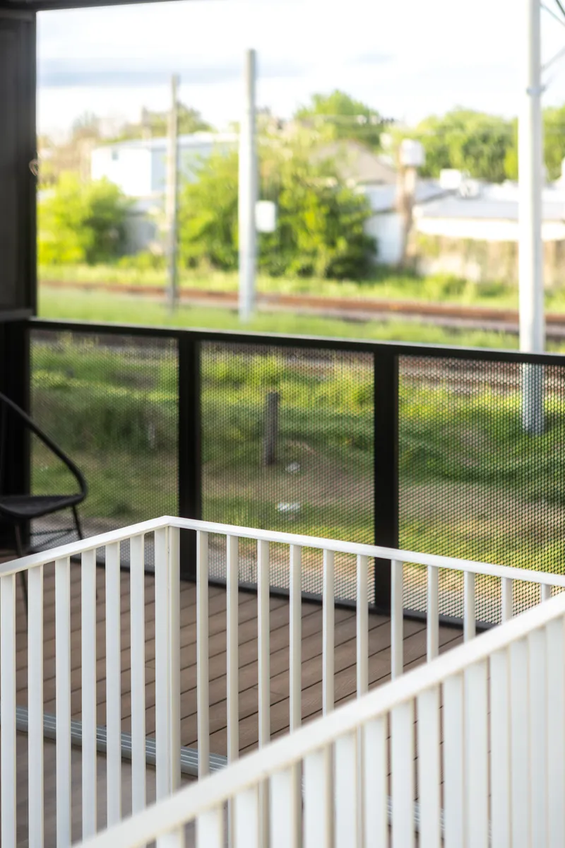 Interior view from the balcony with metal mesh railing overlooking the railway line and vegetation