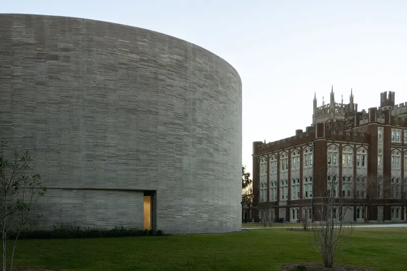Layered grey brick drum with a recessed opening beside a Gothic revival building