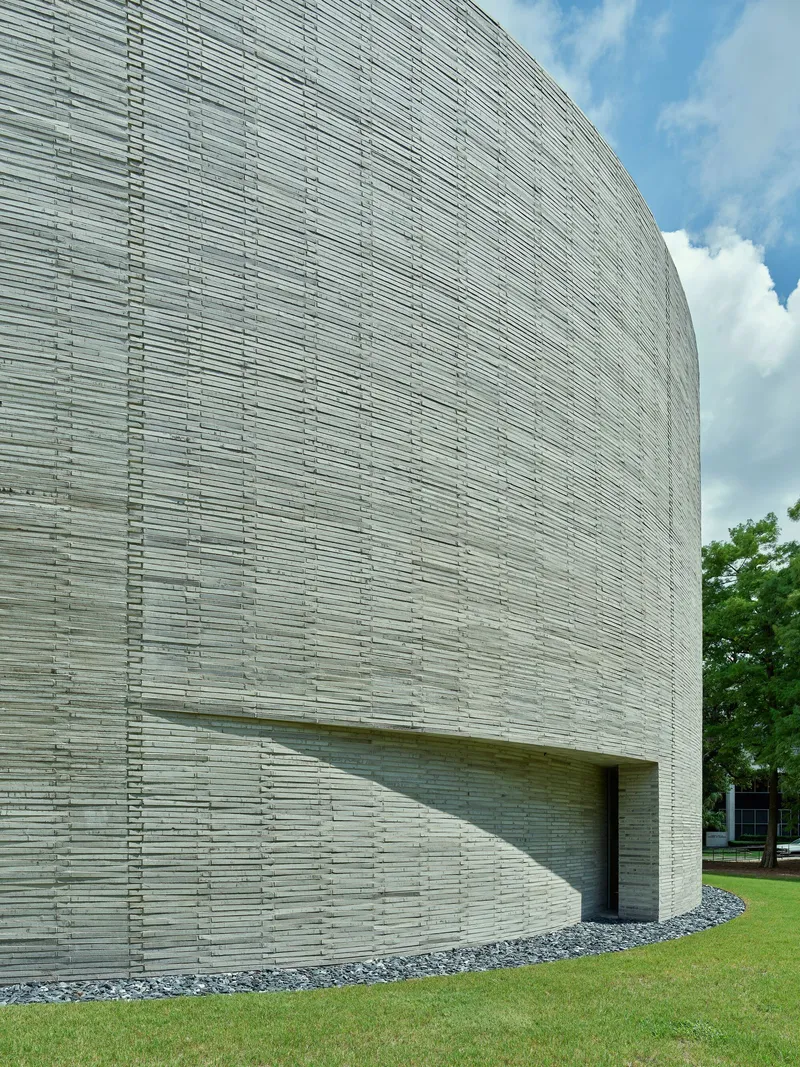 Close-up of the curved brick wall showing recessed entry slot beneath white clouds
