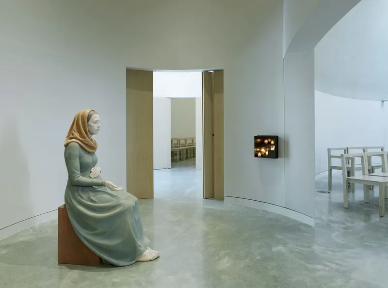 White curved gallery interior with polished concrete floor and seated sculpture facing a doorway