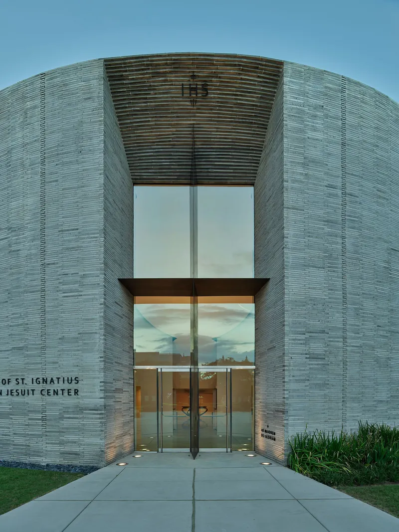 Entrance facade with stacked horizontal brick and tall glass doors under a clear blue sky