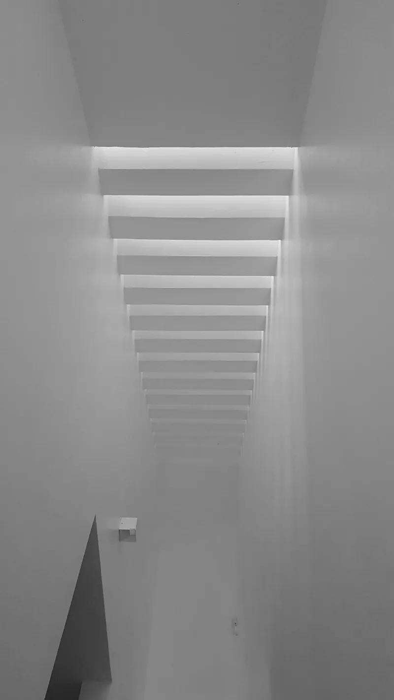 Looking up at a series of horizontal louvers filtering daylight into a white plastered ceiling void