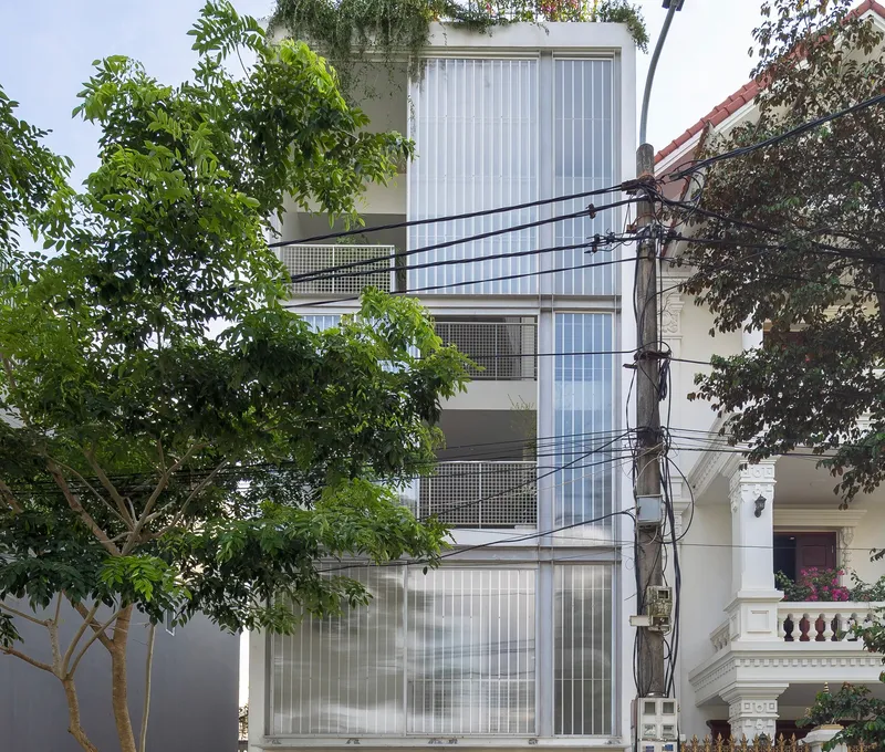 Street view of the vertical corrugated facade with perforated metal balconies framed by neighboring trees
