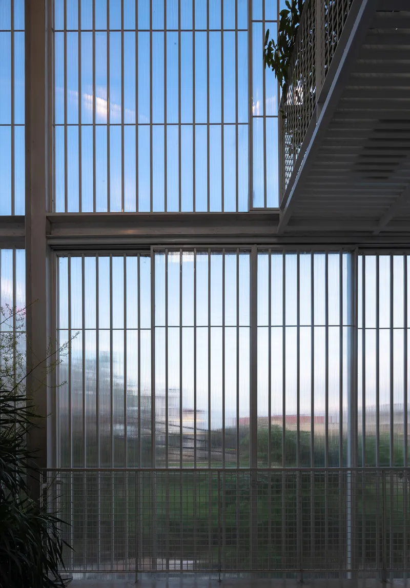 Interior view through vertical polycarbonate louvres showing an open metal mesh walkway and blue sky