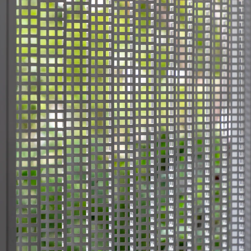 Close-up of perforated metal screen filtering greenery and daylight through square openings
