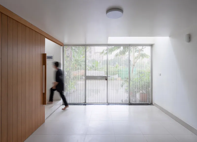 Interior foyer with vertical timber wall and fluted glass entrance doors framing a courtyard with trees