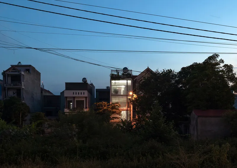 Illuminated tower rising above neighboring rooftops and dense vegetation at twilight with visible overhead cables