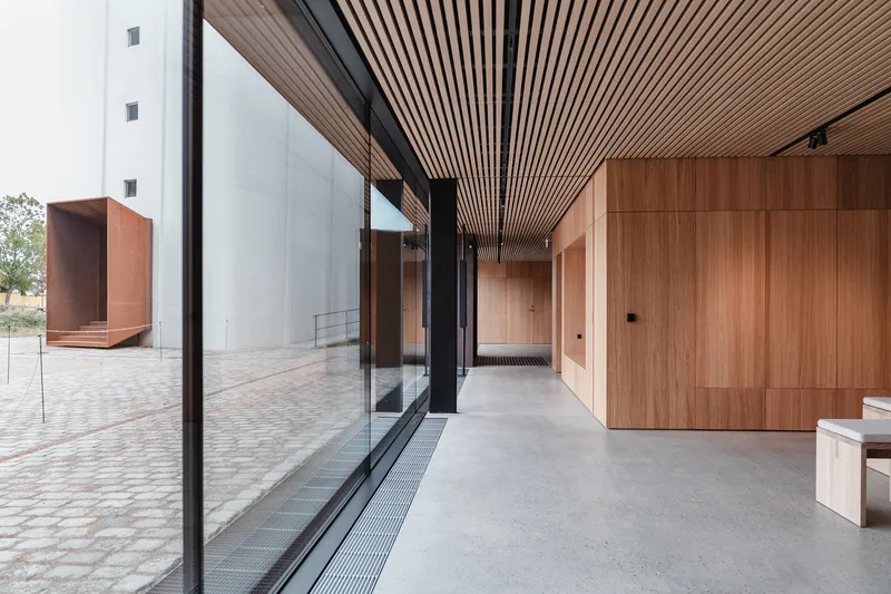 Interior corridor with slatted timber ceiling and full-height glazing overlooking paved courtyard