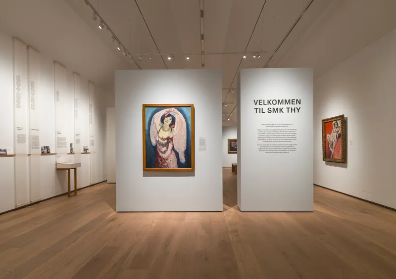 Gallery interior with freestanding white walls displaying framed paintings under track lighting
