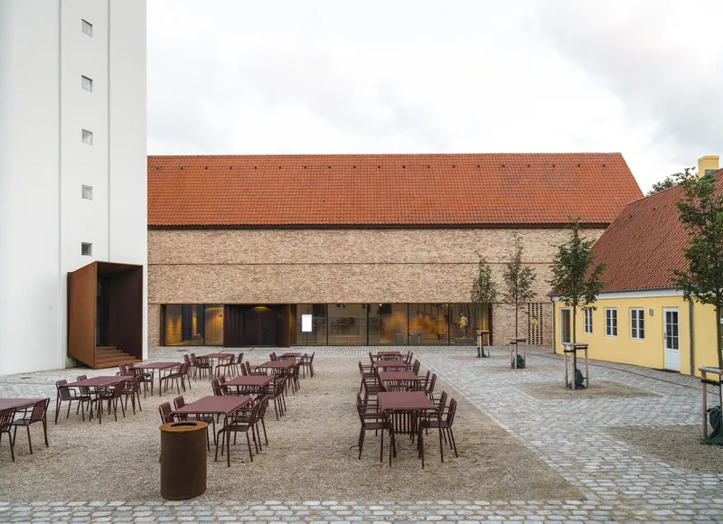 Cobblestone courtyard with burgundy tables and chairs facing a brick building with red tile roof