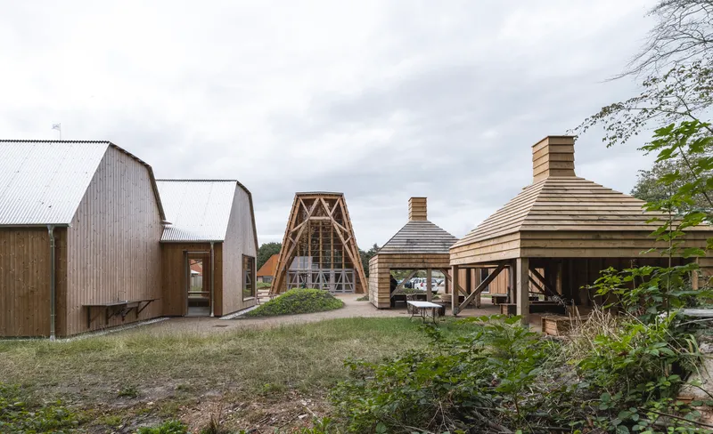 Cluster of timber pavilions with curved and gabled roofs on a grassy hillside under overcast sky