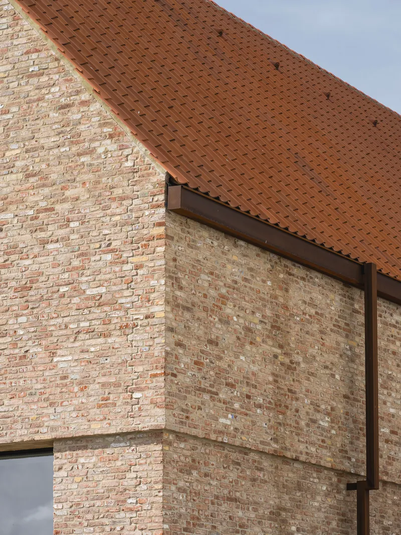 Corner detail of brick masonry gable wall meeting clay tile roof under overcast sky
