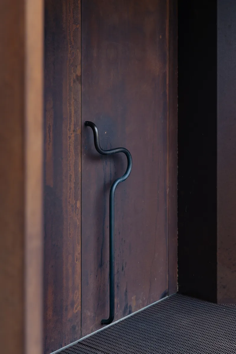 Close-up of forged steel door handle on weathered metal panel beside threshold mat