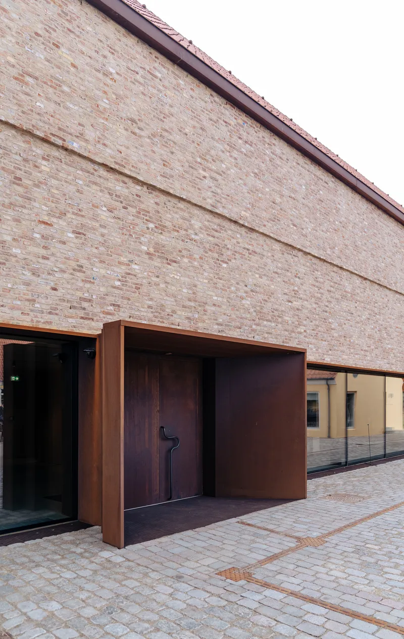 Recessed steel-framed entrance with timber door set into brick facade along paved walkway
