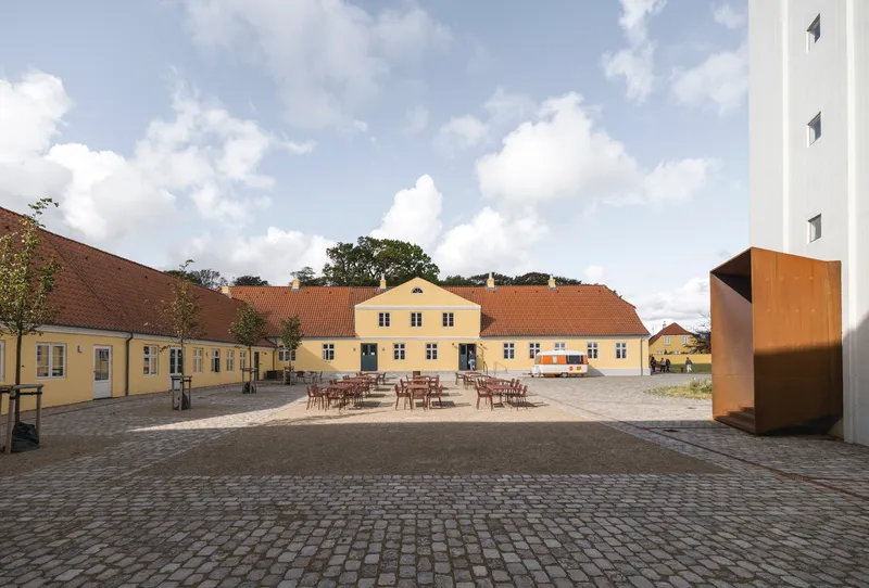 Cobblestone courtyard surrounded by yellow buildings with outdoor seating under a partly cloudy sky