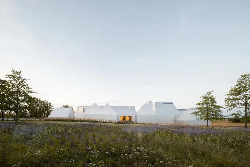 White angular roofscape rising above a field of purple wildflowers at twilight
