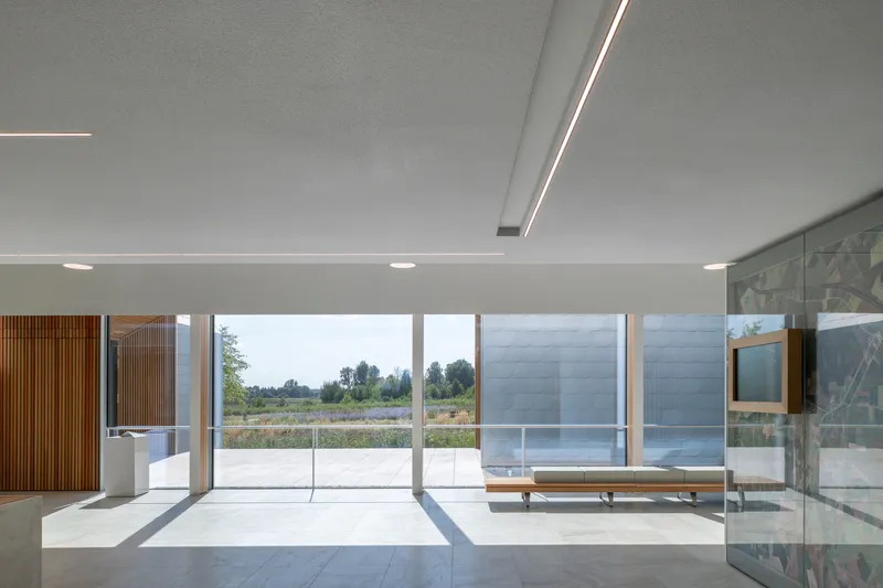 Interior hall with flush ceiling light slots and floor-to-ceiling glazing overlooking an open courtyard