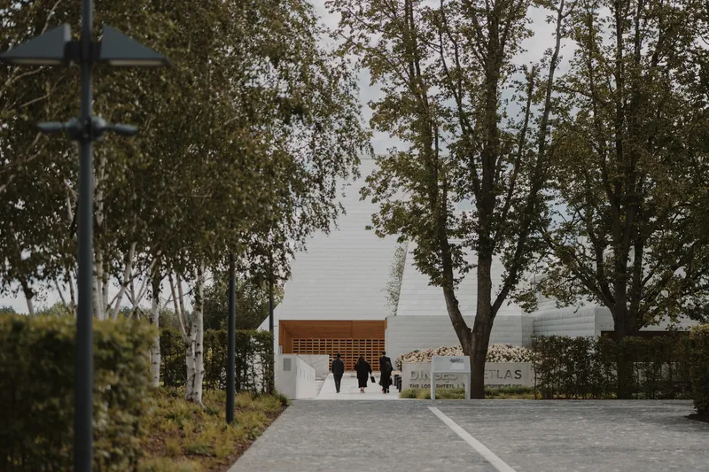 Entrance pathway with visitors approaching the white facade and timber canopy through trees