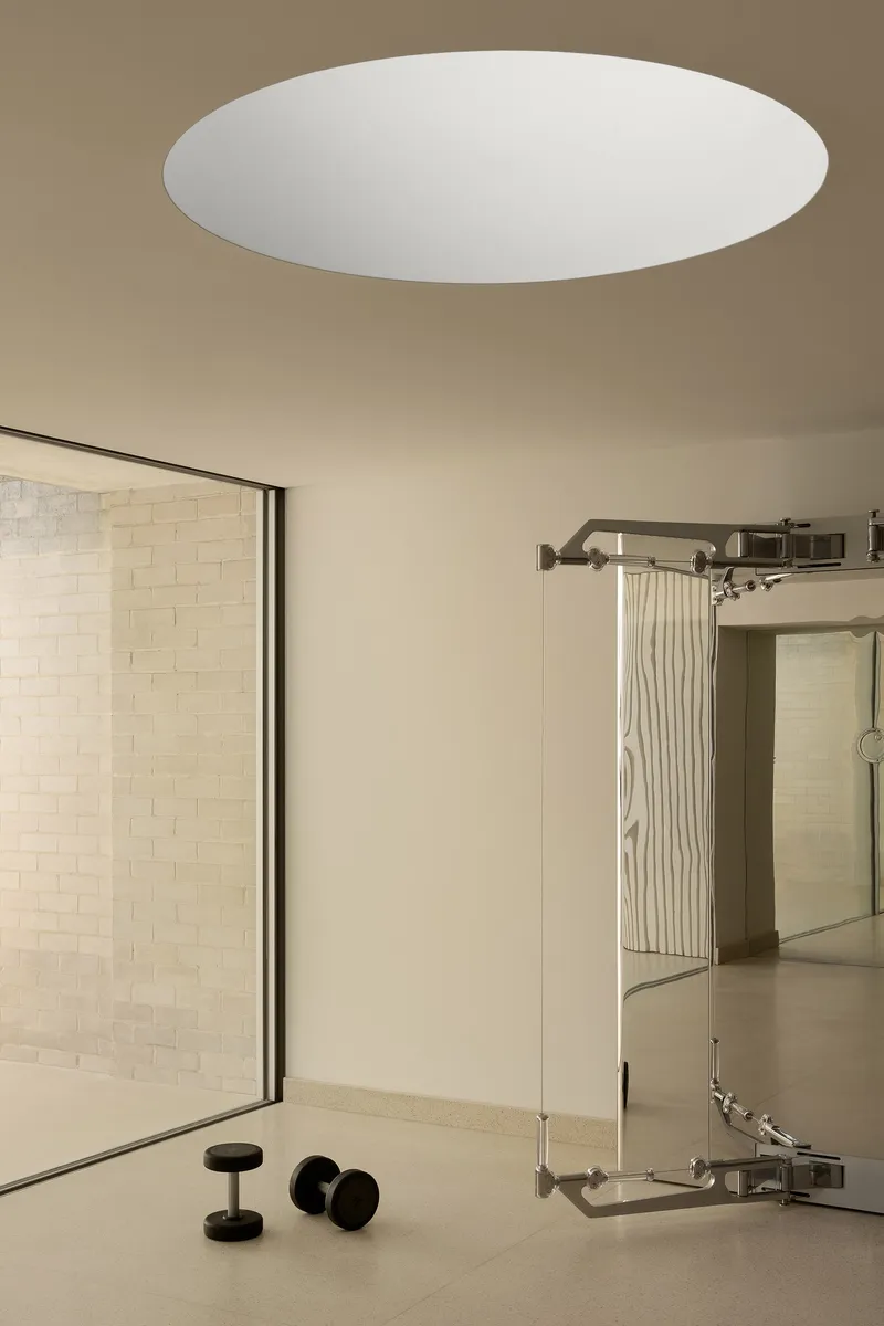 Interior with circular ceiling opening, exercise weights and sliding curtain track beside glazed courtyard wall
