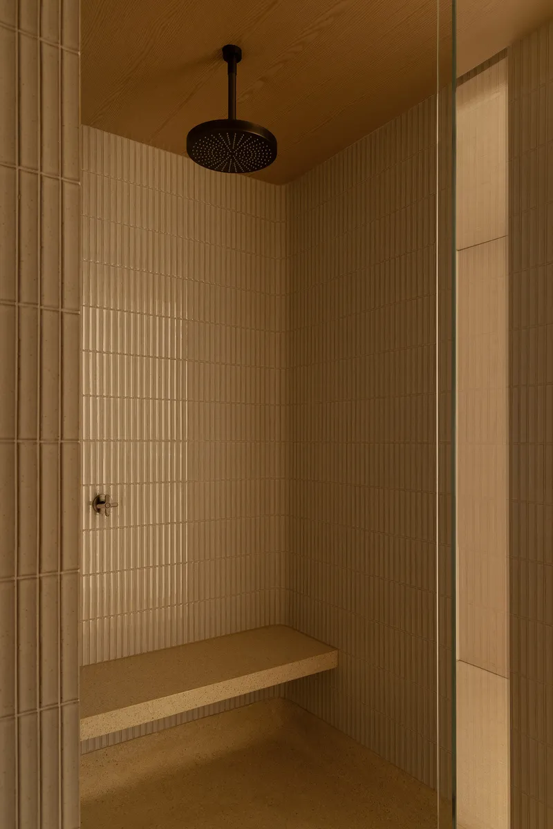 Shower enclosure with vertical ribbed tile walls, ceiling-mounted rainfall head and wooden bench