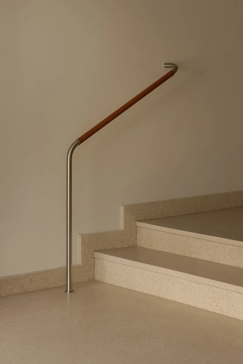 Staircase with terrazzo treads and leather-wrapped handrail terminating at brushed metal base
