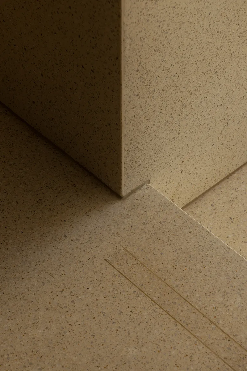 Close-up of terrazzo flooring meeting a wall corner with integrated drainage channel under warm light