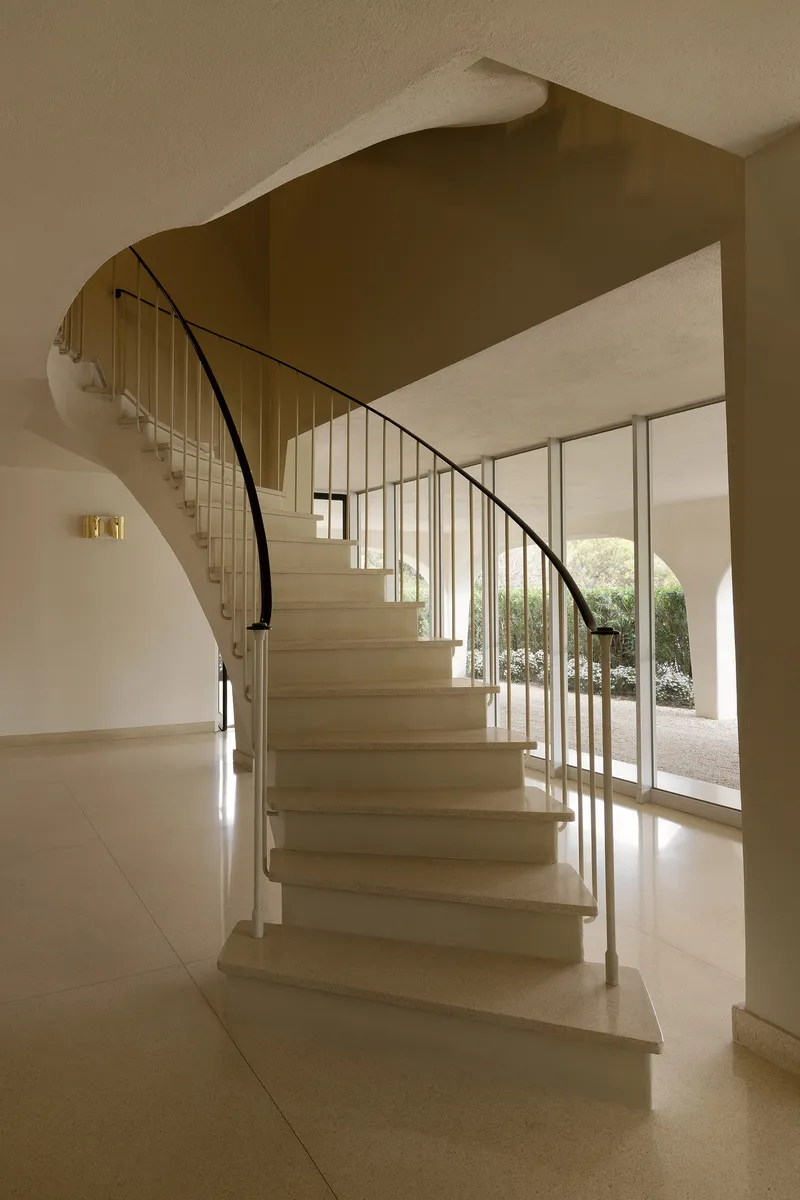 Curved stone staircase with steel rod balustrade and glass doors opening to a courtyard