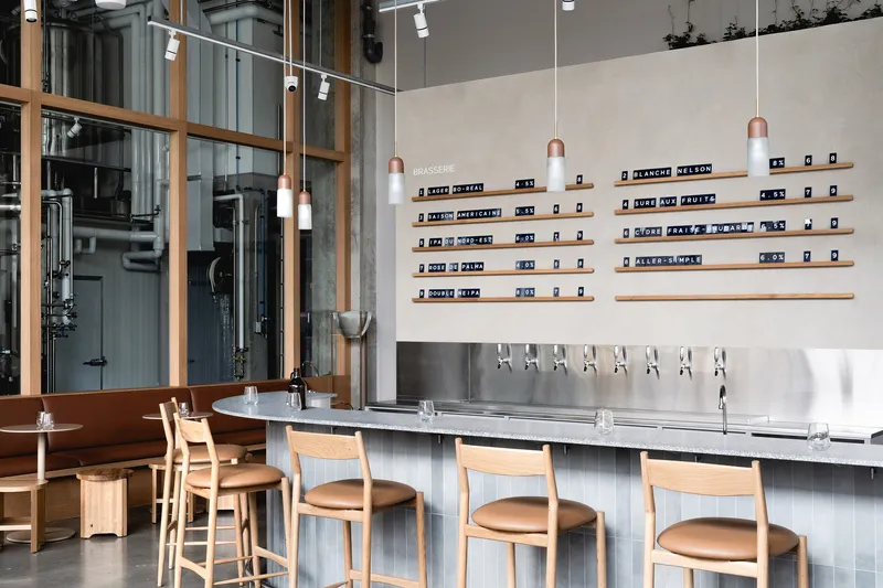 Bar counter with timber shelving displaying labeled bottles, stainless steel taps, and oak stools along fluted base