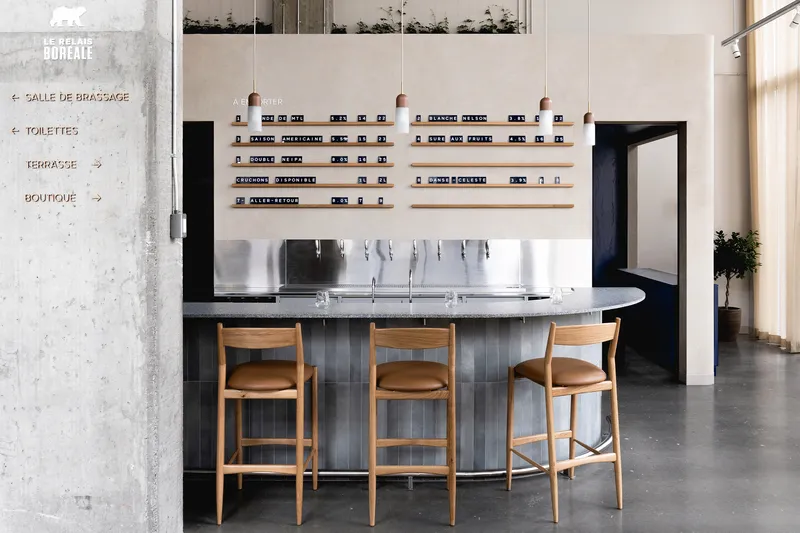 Curved bar with fluted tile base, oak stools, and wall-mounted shelving beside concrete directional signage panel