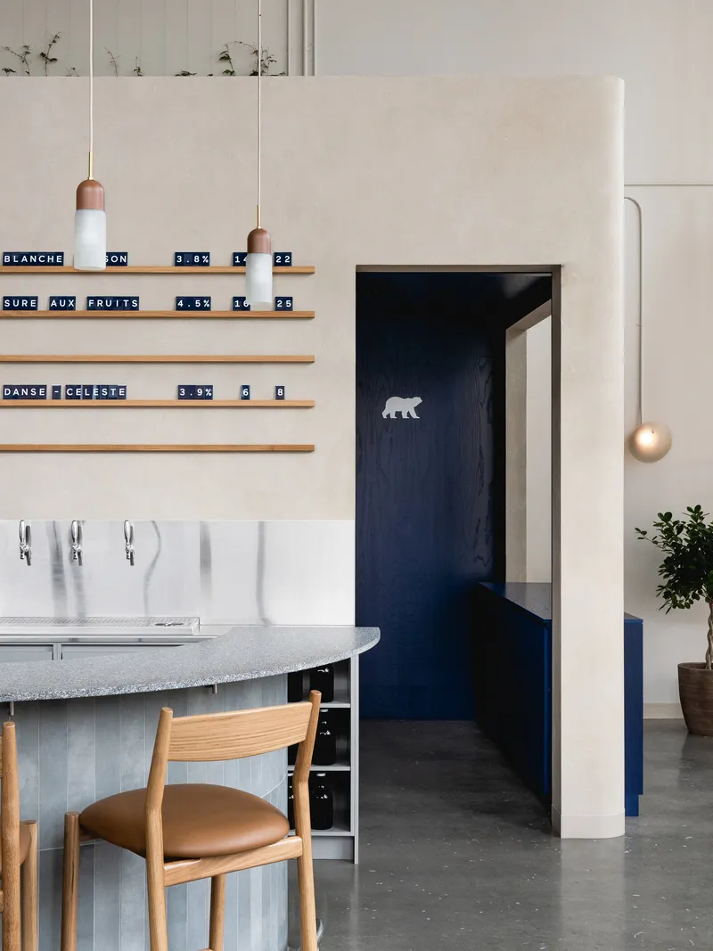 View toward navy-painted doorway with polar bear motif beside curved bar counter and timber shelving with pendant lights