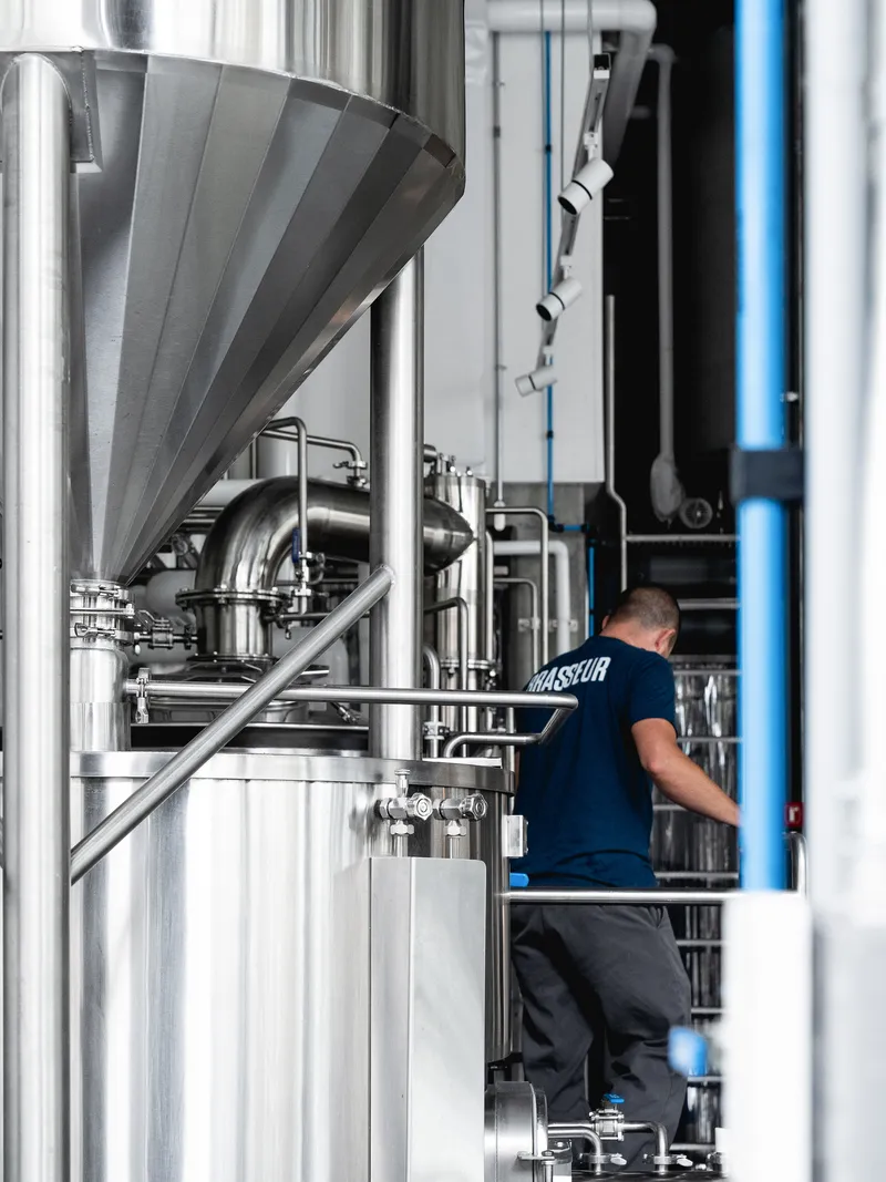 Stainless steel funnel hopper atop fermenting vessels with a worker moving through the production area