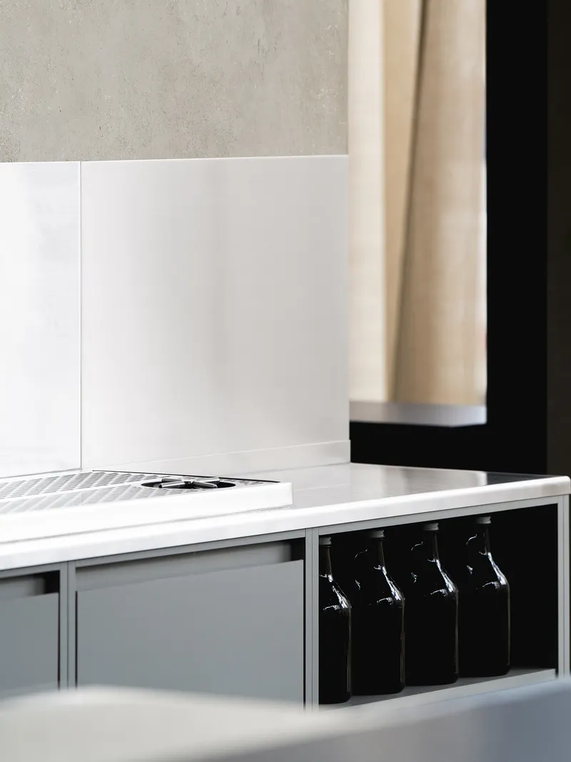 Close-up of a white countertop edge with dark bottles stored in an under-counter recess