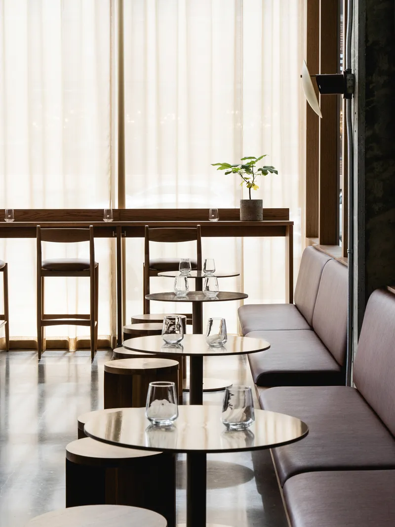 Row of circular tables with glassware along a banquette seat backed by vertical fabric curtains