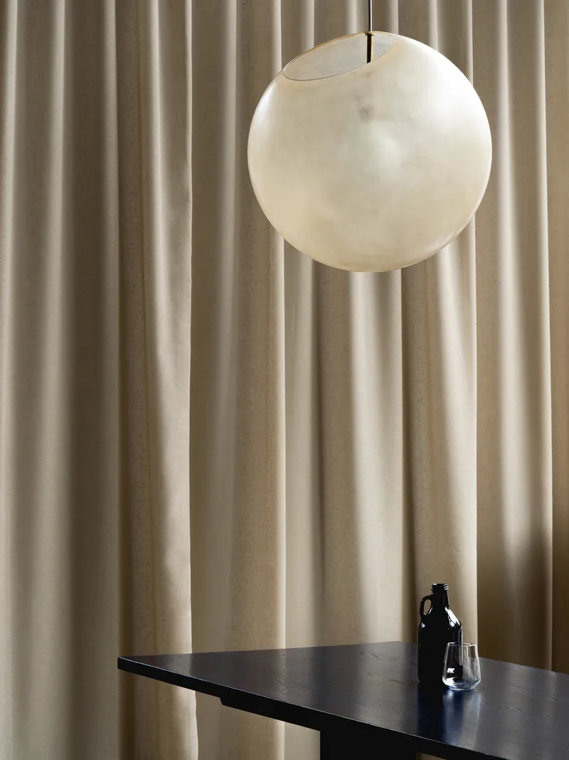 Spherical pendant light suspended above a dark table with bottle and glass against pleated fabric backdrop
