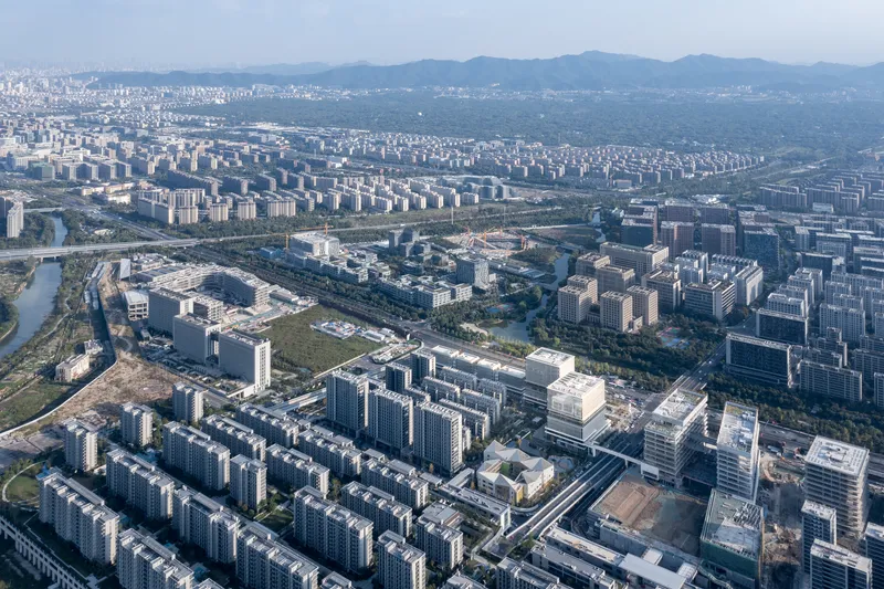 Drone view of large-scale residential district with tower blocks and tree-lined boulevards extending toward mountains