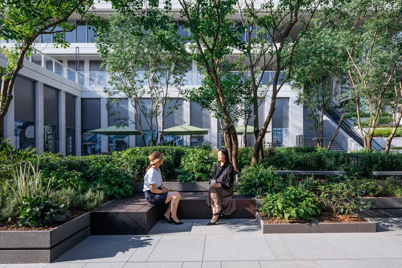 Planted courtyard seating area with two people on timber bench surrounded by trees and low hedges