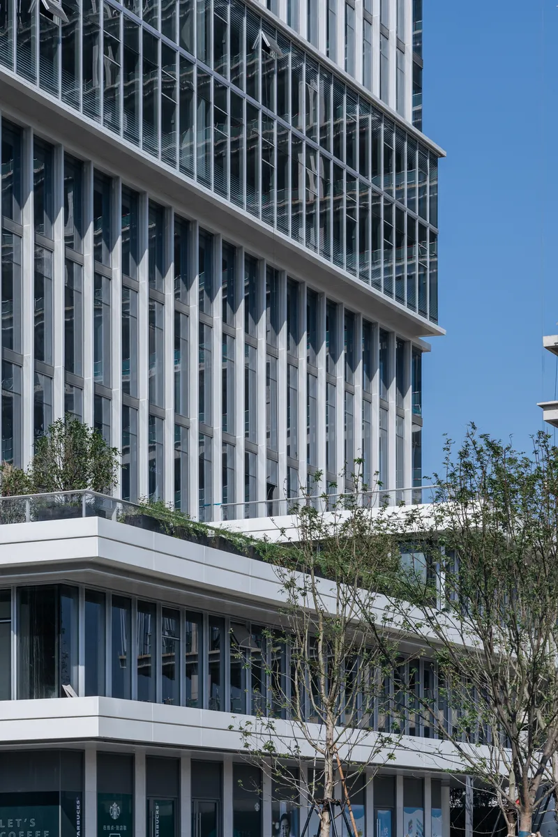 Street view of the vertical white fin facade above planted trees and lower horizontal bands