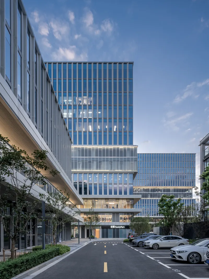 Stacked glass and metal facade volumes viewed from a parking lot at dusk