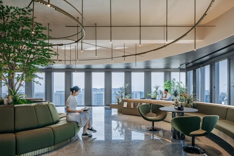 Interior lounge with green seating, terrazzo flooring, suspended circular light fixtures and a person reading