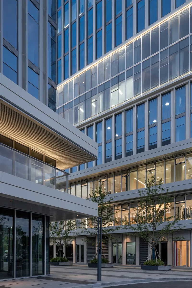 Interior courtyard framed by glass curtain walls and white metal panels with young trees at twilight