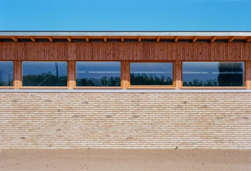 Facade detail showing horizontal timber planks beneath vertical wood cladding and a row of picture windows at dusk