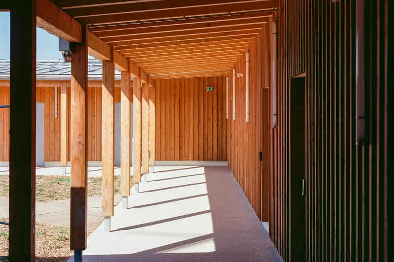 Covered walkway with timber columns casting rhythmic shadows across the polished concrete floor