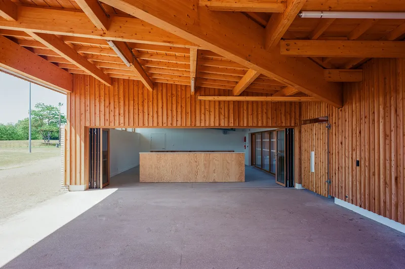 Interior space with exposed timber beams and vertical wood cladding surrounding a plywood service counter