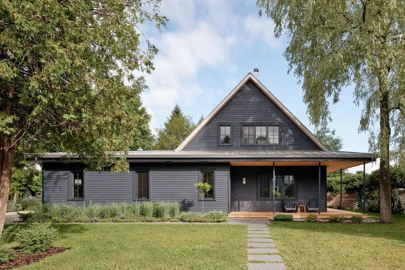 Front facade with dark horizontal cladding, stepped gable roof and a stone pathway through the lawn