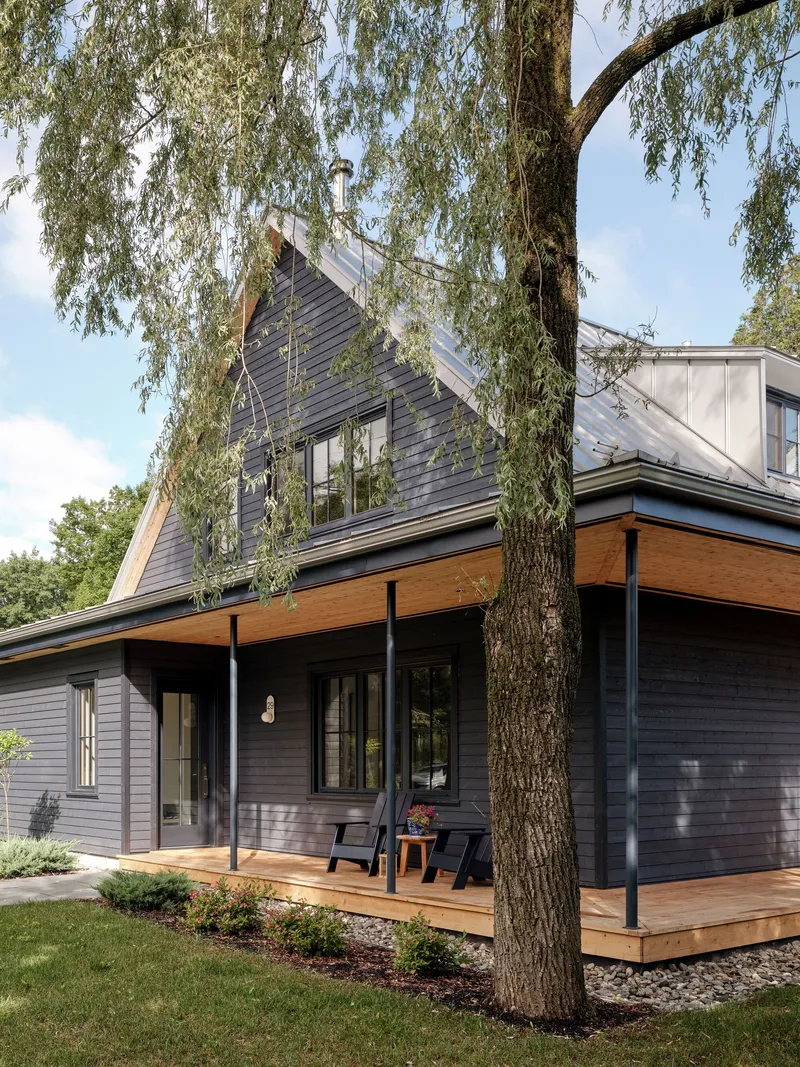 Corner view of the covered porch with timber deck and slender black metal posts framed by a willow tree