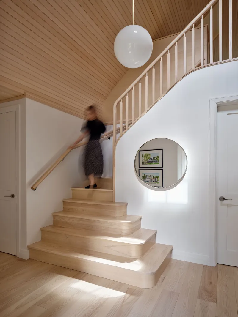 Staircase with circular porthole window in the wall and a figure ascending under the vaulted timber ceiling
