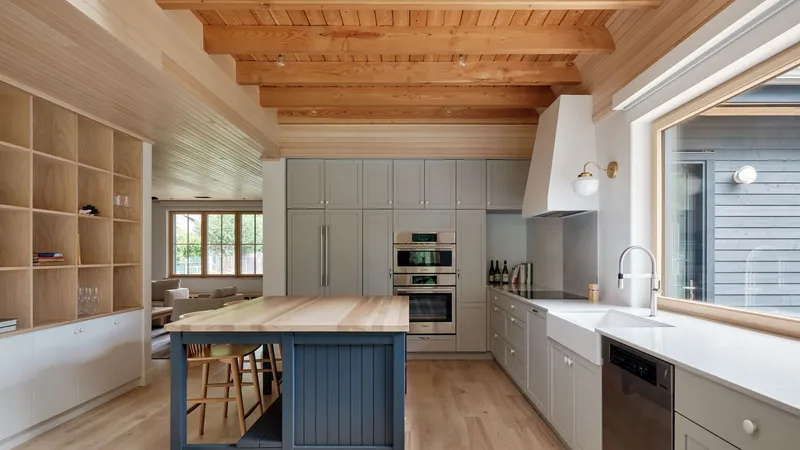 Kitchen with exposed timber ceiling beams and blue-paneled island beneath clerestory windows