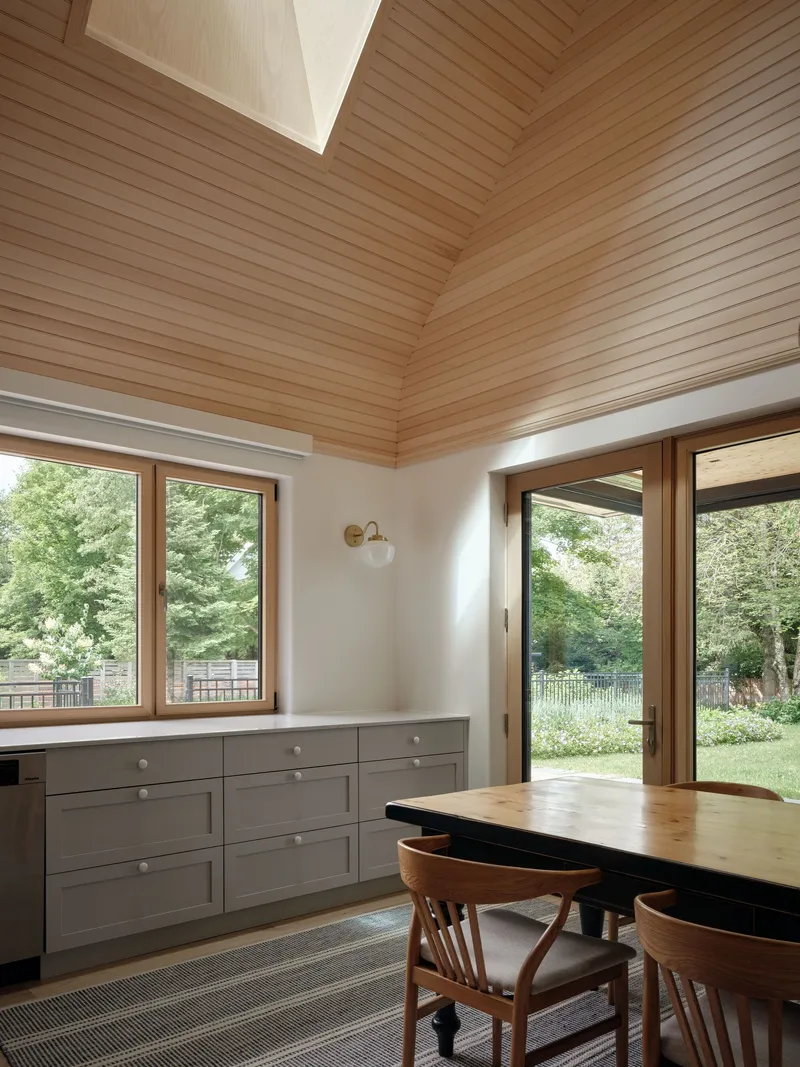 Interior view showing horizontal timber-clad ceiling with skylight and grey cabinetry framing garden view